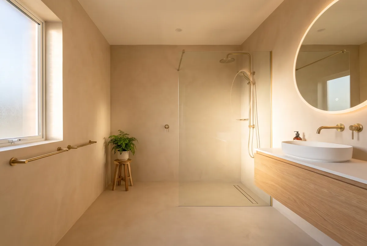 Fugenloses Badezimmer in warmem Beige mit rundem Spiegel und mineralischer Beschichtung